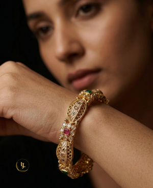 Pair of gold-plated Indian Kada bangles with mint green and pink stones and white enamel Meenakari work on a silk background.