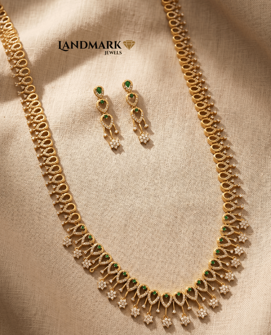 landmark-jewels-gold-plated-long-haram-necklace-and-earring-set-featuring-green-emerald-stones-and-white-crystal-teardrop-motifs-on-a-textured-fabric-background