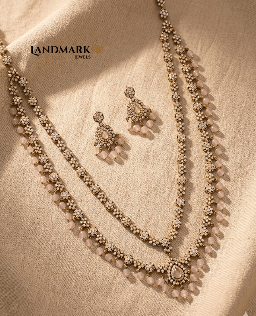 landmark-jewels-antique-gold-plated-double-layer-long-necklace-set-featuring-white-polki-stones-and-light-pink-rose-quartz-beads-with-matching-drop-earrings-on-a-beige-fabric-background