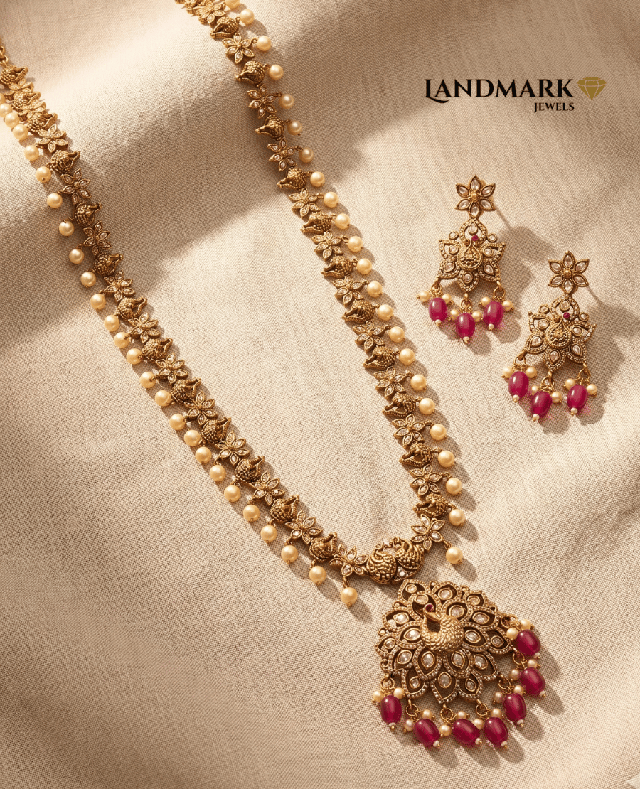 landmark-jewels-antique-gold-plated-long-haram-necklace-and-earring-set-featuring-peacock-motifs-white-stones-and-hanging-ruby-beads-on-a-beige-fabric-background