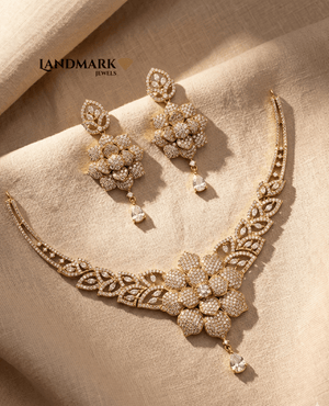 Landmark Jewels gold-plated necklace and earring set featuring a large central flower motif encrusted with white Cubic Zirconia stones on a beige fabric background.