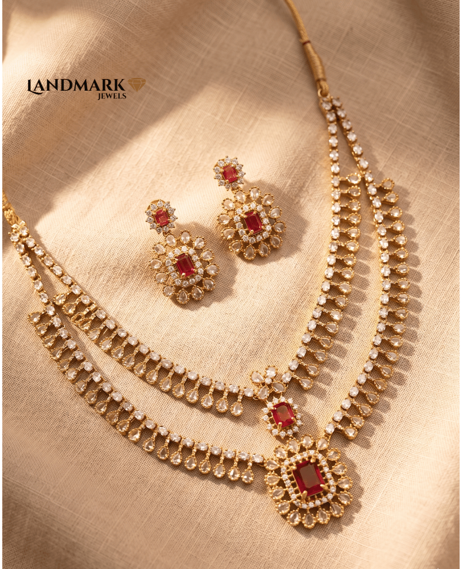 landmark-jewels-two-layer-gold-plated-necklace-set-featuring-red-emerald-cut-rubies-white-ad-stones-and-matching-drop-earrings-on-a-neutral-fabric-background