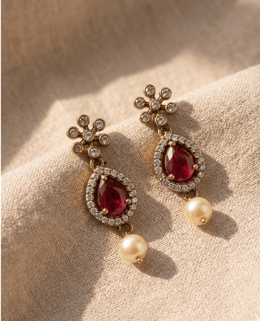 pair-of-landmark-jewels-antique-gold-dangle-earrings-featuring-a-teardrop-red-stone-white-cz-borders-floral-studs-and-hanging-pearls-on-a-beige-fabric-background