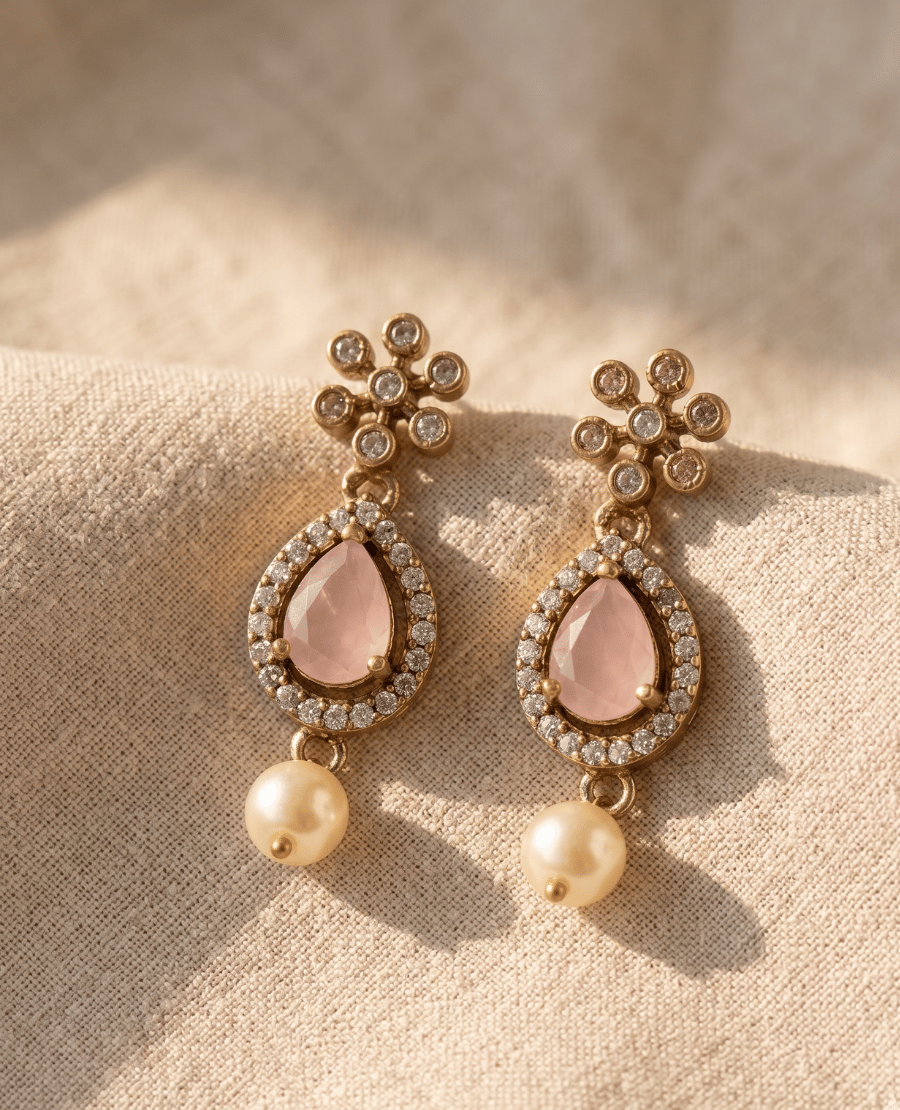 a-pair-of-antique-gold-plated-drop-earrings-featuring-a-faceted-light-pink-stone-in-a-crystal-halo-teardrop-frame-finished-with-a-classic-white-pearl-dangle-underneath