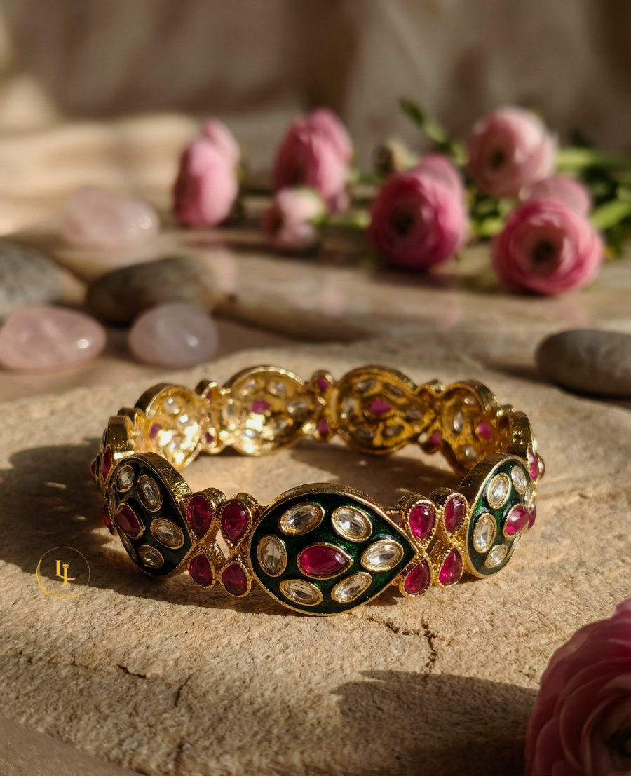 pair-of-gold-plated-indian-bangles-with-ruby-stones-white-polki-crystals-and-black-enamel-work-on-a-floral-background