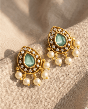 Landmark Jewels mint green pear-shaped cat-eye stone stud earrings bordered with white crystals and small hanging pearls on a beige fabric background.