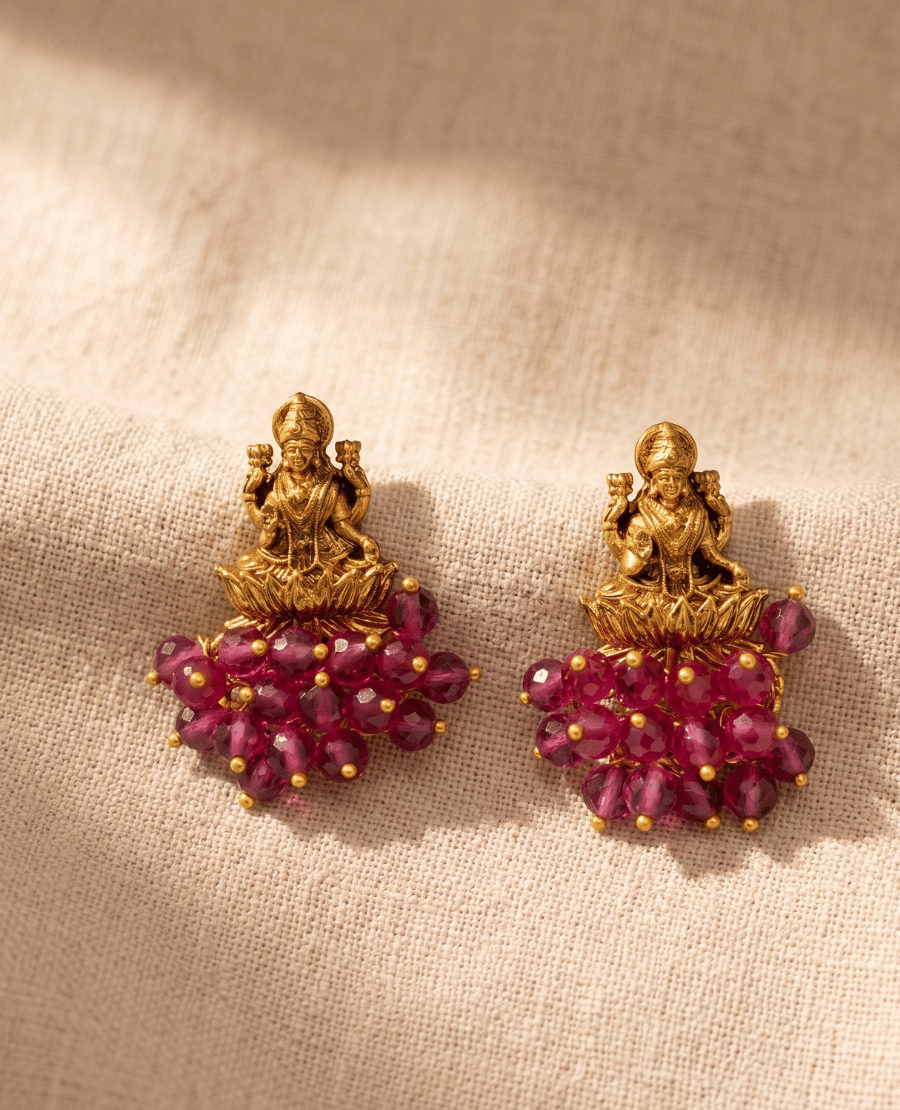 antique-gold-temple-jewelry-earrings-featuring-a-detailed-3d-motif-of-goddess-lakshmi-on-a-lotus-with-a-dense-fringe-of-faceted-maroon-ruby-red-beads