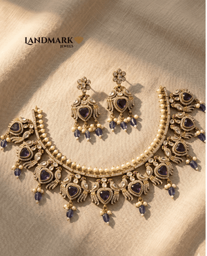 Landmark Jewels imitation jewelry set featuring a gold-toned choker and earrings with purple heart stones, white pearls, and peacock motifs on a beige fabric background.