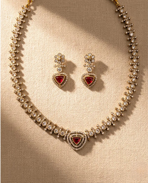 Gold plated ruby red triangular CZ stone necklace set with matching earrings on beige fabric