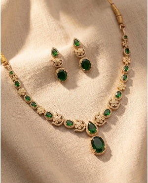 Gold plated emerald green American diamond necklace set with matching drop earrings on beige fabric