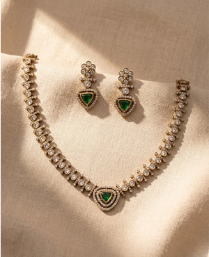 Antique gold plated American diamond choker necklace set with emerald green triangular stone and matching earrings on beige fabric