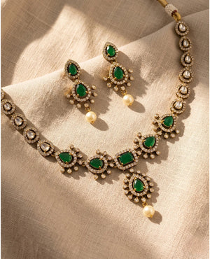 Antique gold emerald green kundan necklace set with pearl drop earrings on beige fabric