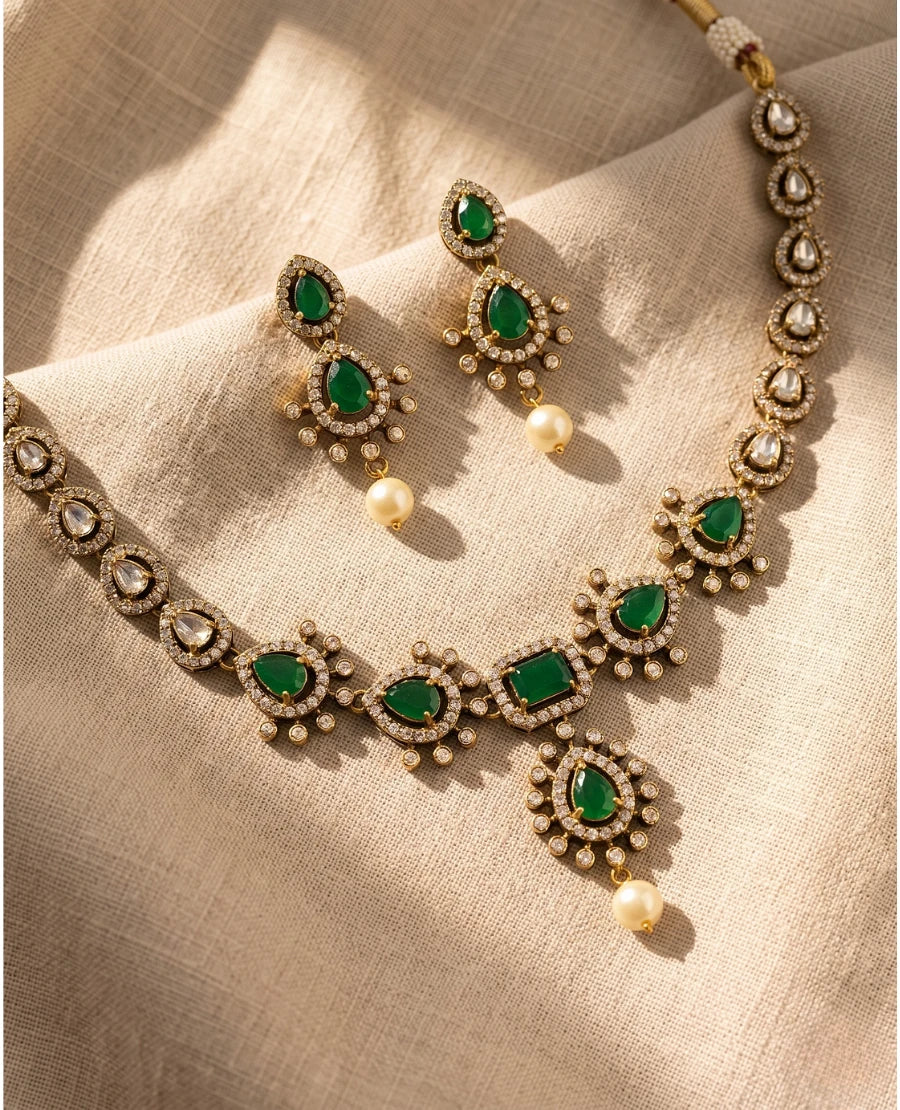 antique-gold-emerald-green-kundan-necklace-set-with-pearl-drop-earrings-on-beige-fabric