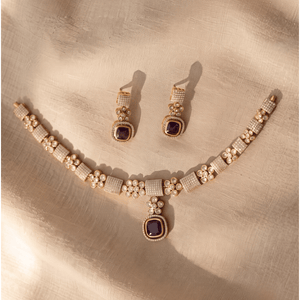 Gold choker necklace with paved crystal squares, floral motifs, and a deep purple Monalisa stone pendant, with matching earrings.