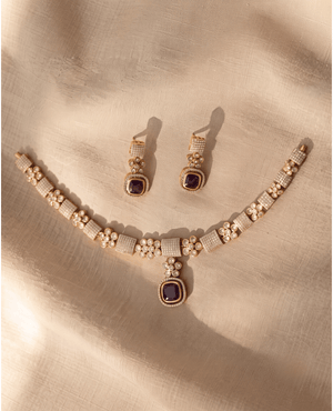 Gold choker necklace with paved crystal squares, floral motifs, and a deep purple Monalisa stone pendant, with matching earrings.
