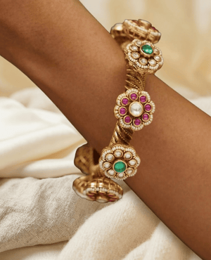 Traditional gold kada bangle with intricate filigree work and embedded green emeralds for weddings.